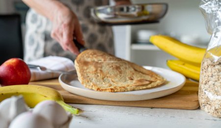 Woman serving a fresh oatmeal pancake out of a pan on a plate for healthy breakfast