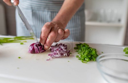 Woman preparing fresh herbs and onions on a cutting board in the kitchen