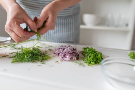 Mujer preparando hierbas frescas y cebollas en una tabla de cortar en la cocina