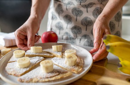 Woman with fresh and healthy oatmeal pancake with bananas for breakfast in the kitchen