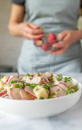 Téléchargez les photos : Salade de pommes de terre saine avec sauce au yaourt, radis, oignons, cornichons et ciboulette dans un bol. - en image libre de droit