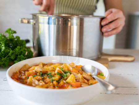 Soupe de légumes végétalien ou ragoût avec haricots blancs sur une assiette avec casserole et femme sur fond de cuisine.