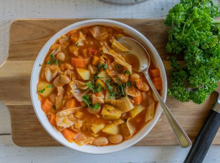 Soupe au chou avec haricots blancs et légumes. Nourriture végétalienne saine. servi prêt à manger dans un bol avec cuillère sur une planche à découper. Vue de dessus de table
