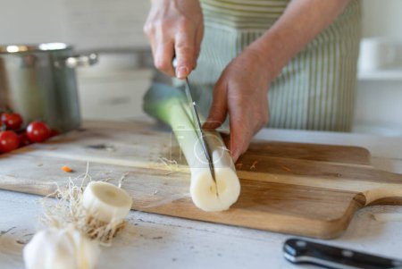 Couper le poireau le long chemin pour le nettoyer correctement par les mains de femmes dans la cuisine.