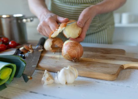 Persona pelando una cebolla en una tabla de cortar en la cocina