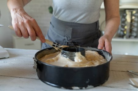 Teig oder Teig in einer Backform von Frauenhänden glätten. Ein Bündel Kuchen in der Küche