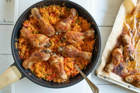 Healthy balkan rice with oven baked chicken drumsticks in a frying pan. Glutenfree dinner or lunch on light table background from above.