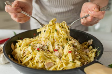Nudelpfanne aglio e olio mit Hühnerbrust von Frauenhänden in der Küche zubereiten