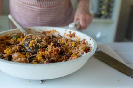 Foto de Mujer en la cocina con un plato de arroz fresco y saludable con frijoles, maíz, pimientos, cebollas, tomates y hierbas. - Imagen libre de derechos
