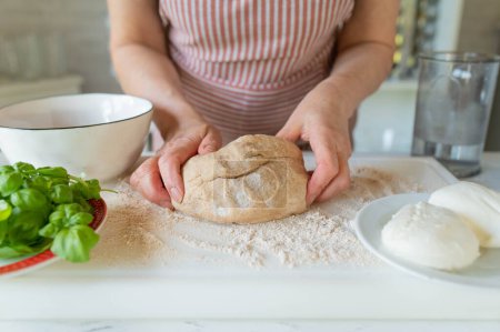 Womans hands holding a fresh kneaded whole wheat pizza dough  on floured surface with ingredients for making a healthy pizza.