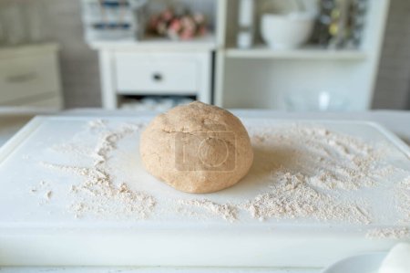 Ball of fresh whole wheat pizza dough on floured surface in the kitchen. Healthy eating background with copy space.