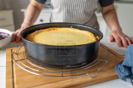 Fresh baked cheesecake in a round baking pan  on a cooling rack in the kitchen