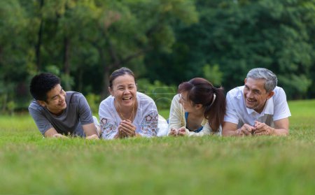 Foto de Grupo de familia asiática con padre, madre, hijo e hija acostados juntos en el césped y riendo en el parque público durante la actividad de fin de semana para una buena salud mental y recreación - Imagen libre de derechos