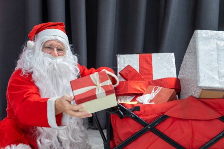 Foto de Santa Claus está sosteniendo la caja de regalo de Navidad con carro completamente cargado para la celebración de la temporada y feliz año nuevo concepto de evento - Imagen libre de derechos