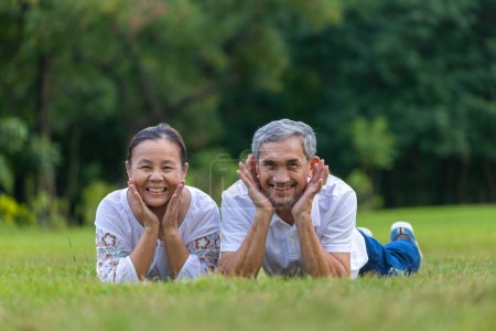 Téléchargez les photos : Portrait de couple asiatique aîné allongé sur l'herbe dans le parc public regardant la caméra avec une bonne santé mentale pour la longévité et le concept de mariage heureux - en image libre de droit