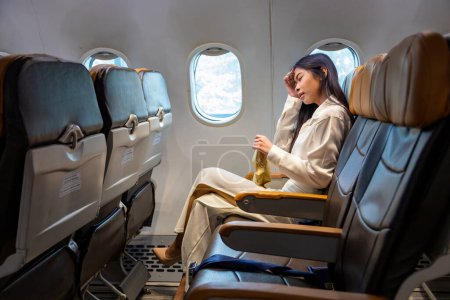 Téléchargez les photos : Femme asiatique se sent étourdi et tenant à vomir sac pendant le vol dans l'avion en raison du mouvement et le mal des transports qui causent des étourdissements pour l'aérobie et le concept de transport - en image libre de droit