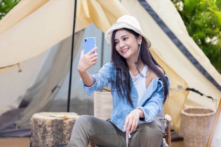 Téléchargez les photos : Femme asiatique utilise le téléphone mobile pour prendre des photos selfie à sa tente tout en campant en plein air pendant l'heure d'été dans le parc national pour l'aventure et les voyages actifs - en image libre de droit