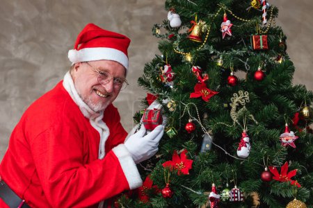 Photo for Senior caucasian man celebrating Christmas in happiness and excitement while holding the present beside the decorated christmas tree - Royalty Free Image