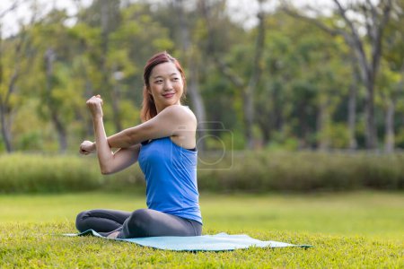 Photo for Asian woman relaxingly practicing arm and shoulder stretching yoga inside the public park for cool down after exercise inside the public park - Royalty Free Image