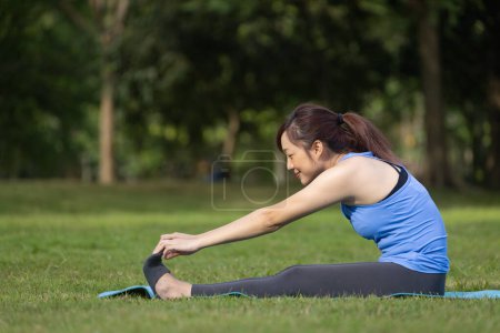 Photo for Asian woman relaxingly practicing forward bending yoga or hamstring stretching yoga for cool down after exercise inside the public park - Royalty Free Image