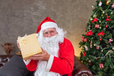 Photo for Santa Claus is holding christmas present box with fully decorated chrsitmas tree for season celebration and happy new year event concept - Royalty Free Image