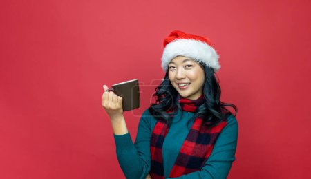 Foto de Mujer asiática bastante sonriente en suéter de Navidad caliente y sombrero de santa está teniendo chocolate caliente sobre fondo rojo para la celebración de la temporada - Imagen libre de derechos