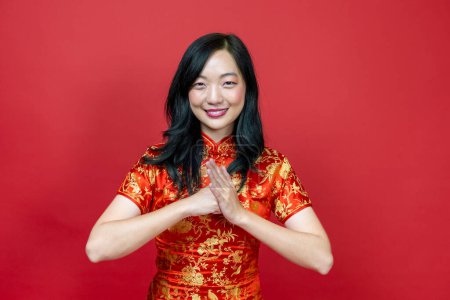 Foto de Mujer china asiática con cheongsam rojo o qipao haciendo gesto respetuoso cortés para desear la buena suerte y prosperidad en las vacaciones de celebración de Año Nuevo chino aislado en el fondo rojo - Imagen libre de derechos