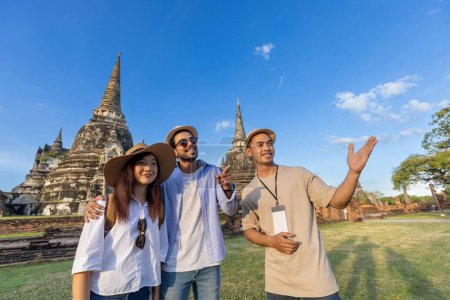 Photo for Thai local tour guide is explaining the history of old Siam to the couple of tourist on their backpacker honeymoon travel to ancient temple of Ayutthaya, Thailand - Royalty Free Image