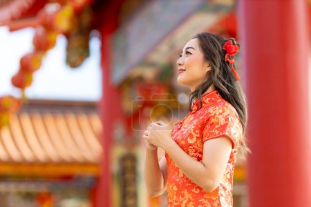 Foto de Asian woman in red cheongsam qipao dress is making a wish to ancestral god inside Chinese Buddhist temple during lunar new year for  for best wish blessing and good luck - Imagen libre de derechos