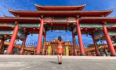 Photo for Rear view of Asian woman in red cheongsam qipao dress is visiting the Chinese Buddhist temple during lunar new year for traditional culture concept - Royalty Free Image