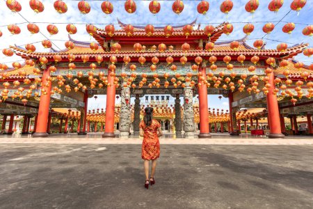 Foto de Rear view of Asian woman in red cheongsam qipao dress is visiting the Chinese Buddhist temple during lunar new year for traditional culture - Imagen libre de derechos
