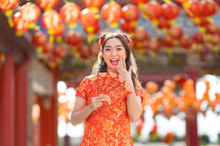 Photo for Asian woman in red cheongsam qipao dress is holding red envelope for money saying 'May you have great luck and profit' inside Chinese Buddhist temple during lunar new year for best wish blessing - Royalty Free Image