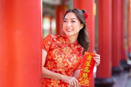 Foto de Asian woman in red cheongsam qipao dress is holding blessing fortune card saying 'to be blessed by a lucky star' inside Chinese Buddhist temple during lunar new year for best wish and good luck concept - Imagen libre de derechos
