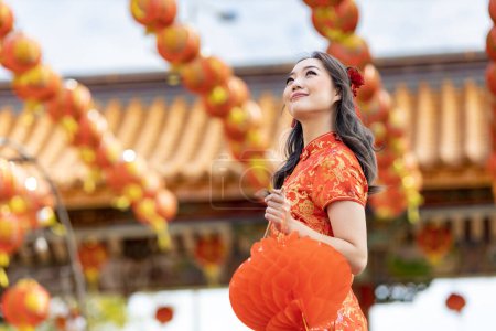 Foto de Asian woman in red cheongsam qipao dress holding lantern while visiting the Chinese Buddhist temple during lunar new year for traditional culture - Imagen libre de derechos