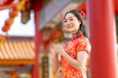 Foto de Asian woman in red cheongsam qipao dress is making a wish to ancestral god inside Chinese Buddhist temple during lunar new year for  for best wish blessing and good luck concept - Imagen libre de derechos