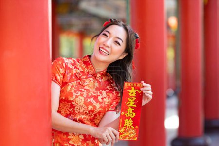 Foto de Asian woman in red cheongsam qipao dress is holding blessing fortune card saying 'to be blessed by a lucky star' inside Chinese Buddhist temple during lunar new year for best wish and good luck - Imagen libre de derechos