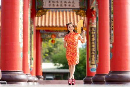 Foto de Asian woman in red cheongsam qipao dress holding paper fan while visiting the Chinese Buddhist temple during lunar new year for traditional culture - Imagen libre de derechos