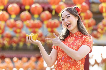 Téléchargez les photos : Asian woman in red cheongsam qipao dress is holding ancient gold money inside Chinese Buddhist temple during lunar new year for best wish blessing and good luck - en image libre de droit