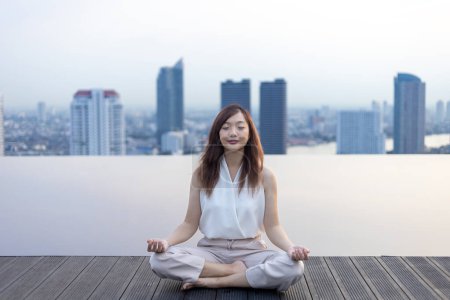 Téléchargez les photos : Femme pratiquant la méditation relaxante sur le toit de la piscine avec vue sur le bâtiment urbain skyline pour atteindre le bonheur de la paix intérieure sagesse - en image libre de droit