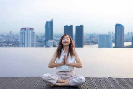 Téléchargez les photos : Femme pratiquant la méditation relaxante sur le toit de la piscine avec vue sur le bâtiment urbain skyline pour atteindre le bonheur de la paix intérieure sagesse - en image libre de droit