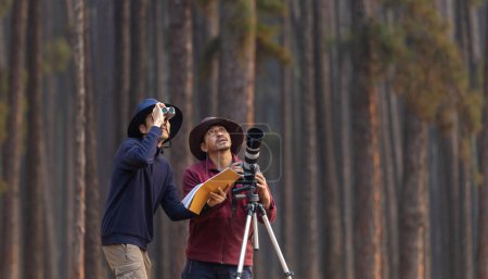 Foto de Equipo del naturalista asiático mirando a las nuevas especies de aves descubiertas mientras explora en el bosque de pinos para estudiar y localizar la rara diversidad biológica y ecologista en el estudio de campo - Imagen libre de derechos