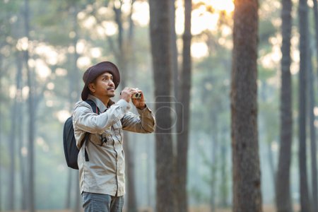 Photo for Bird watcher is looking through binoculars while exploring in the pine forest for surveying and discovering the rare biological diversity and ecologist on the field study - Royalty Free Image
