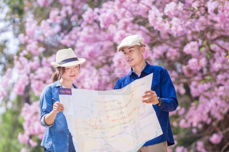 Photo for Asian couple tourist holding city map while walking in the park at cherry blossom tree during spring sakura flower festival - Royalty Free Image