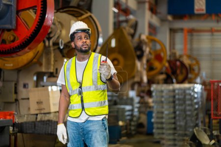 Téléchargez les photos : Travailleur industriel afro-américain utilise talkie walkie tout en travaillant à l'intérieur de la tôle galvanisée usine de toit pour l'industrie de la sécurité - en image libre de droit