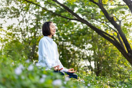 Foto de Mujer asiática está practicando relajadamente yoga meditación en el bosque lleno de flores silvestres en verano para alcanzar la felicidad de la paz interior sabiduría con la luz de la mañana para la mente sana y el concepto del alma - Imagen libre de derechos