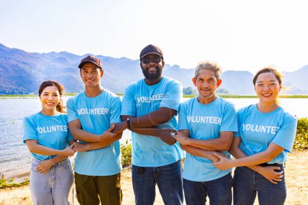 Foto de El equipo de trabajadores voluntarios jóvenes y diversos disfruta del trabajo social caritativo al aire libre en el proyecto de limpieza de la playa usando una camiseta azul mientras se une a la mano para ensamblar la unidad - Imagen libre de derechos