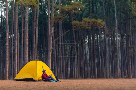 Téléchargez les photos : Camper seul toute la nuit tout en étant assis à côté de la tente au camping dans la forêt de pins tout en écrivant journal pour la liberté, la solitude, escapade de détente paisible à la nature sauvage et thérapie de guérison de la nature - en image libre de droit
