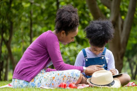 Photo for African American mother is teaching her young daughter to read while having a summer picnic in the public park for education and happiness - Royalty Free Image