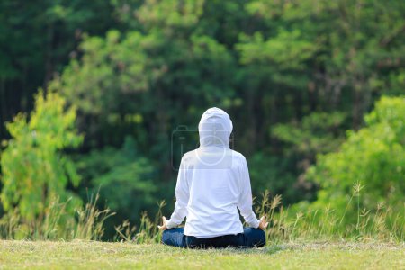 Photo for Rear view of woman in hoodie is relaxingly practicing meditation yoga in forest full of grass meadow in the summer to attain happiness from inner peace wisdom with morning light for healthy mind and soul - Royalty Free Image