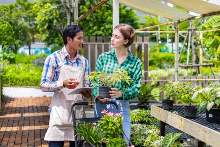 Photo for Young caucasian customer is asking the nursery owner about the exotic plant with shopping cart full of summer plant for weekend gardening and outdoor - Royalty Free Image
